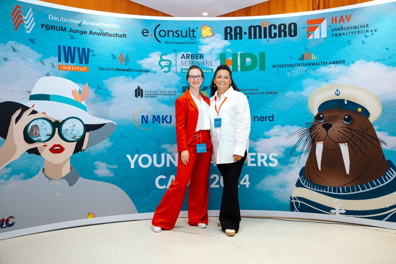 Nasita Mika und Simone Krämer von RA-MICRO vor der Sponsorenleinwand des Young Lawyers Camp 2024.